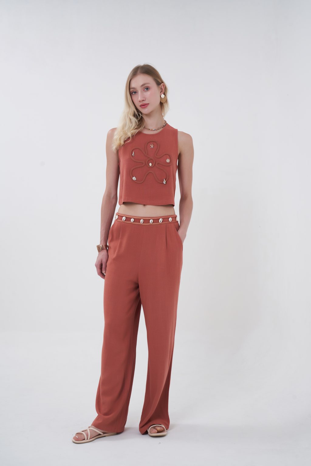 A warm-weather statement piece, the Terra Shell Embellished Crop Top features a textured woven fabric in a rich earthy hue, designed with a relaxed sleeveless silhouette and cropped length for effortless styling. The front is delicately adorned with shell accents arranged in an organic motif, adding a subtle coastal touch while keeping the look modern and elevated. Lightweight and breathable, it’s perfect for sunny days, vacations, or relaxed resort evenings.
